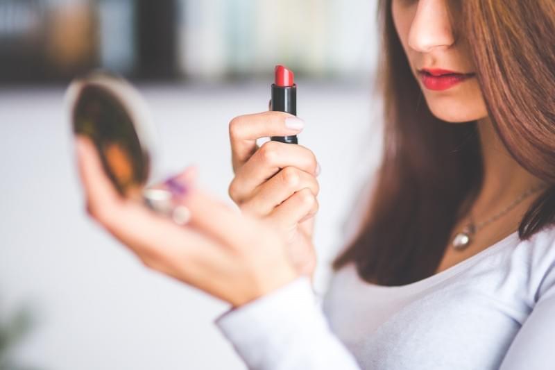 woman-with-brown-hair-doing-lipstick-and-holding-little-mirror